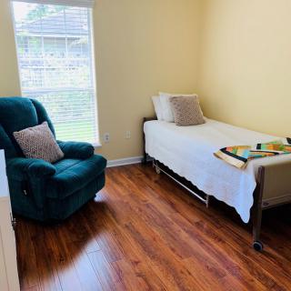 A cozy bedroom with a single bed, armchair, and hardwood flooring.
