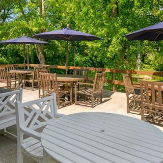 A sunny outdoor patio with tables, chairs, and umbrellas, surrounded by lush greenery.