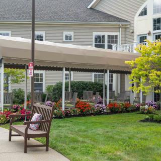 A peaceful garden area with a bench, canopy, and colorful flowers outside a building.