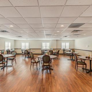 An empty dining room with hardwood floors, arranged tables and chairs, and windows letting in natural light.