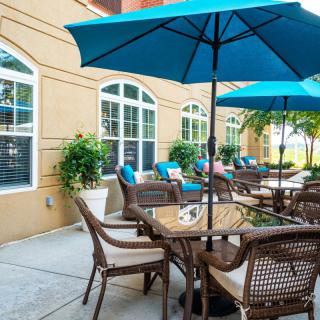 An outdoor patio area with tables, chairs, and blue umbrellas alongside a building.