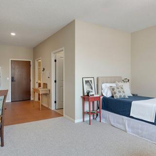 A cozy and minimalist bedroom featuring a single bed, small side table, and wooden floor with neutral tones.