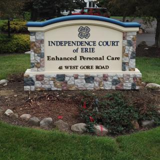 A stone sign for Independence Court of Erie Enhanced Personal Care on West Gore Road, surrounded by landscaping.