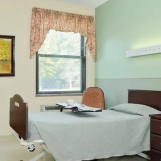 A simple hospital room with a single bed, a window, and a nightstand.