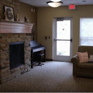 A cozy living room with a stone fireplace, piano, and sofa.
