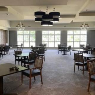 An empty dining room with neatly arranged tables and chairs, featuring large windows and elegant chandeliers.