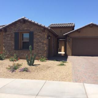 A single-story brick house with a desert landscape and attached garage.