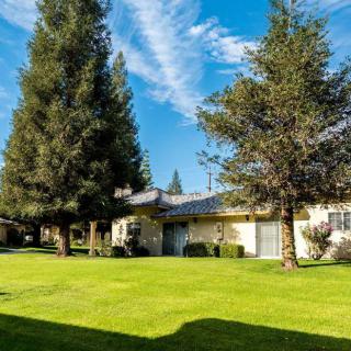 A suburban house with a well-maintained lawn and tall trees under a clear sky.