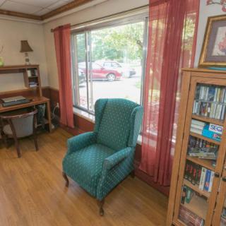 A cozy living room corner with an armchair by the window, a bookshelf, and a small desk.