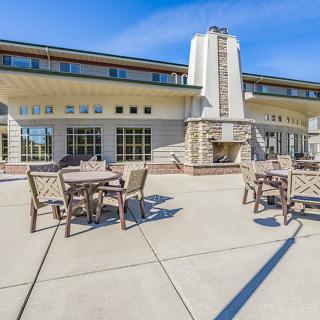 A spacious outdoor patio with tables and chairs set against a large, modern building under a clear blue sky.