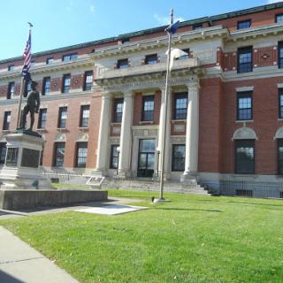 A grand building featuring a statue in front, surrounded by well-maintained grass and flags.