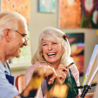 Two seniors enjoying a painting class together, sharing a joyful moment.