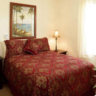 A cozy bedroom with a red floral bedspread and a beach-themed painting.