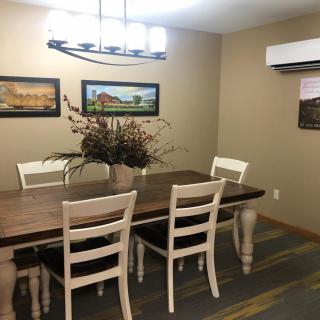 A cozy dining room with a wooden table and six chairs, adorned with wall art and a central plant decoration under modern lighting.