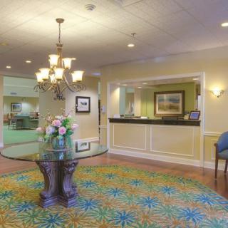 A brightly lit hotel lobby with a reception desk and a floral arrangement on a round table.