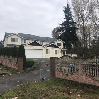 A two-story house with a fenced driveway on a cloudy day.