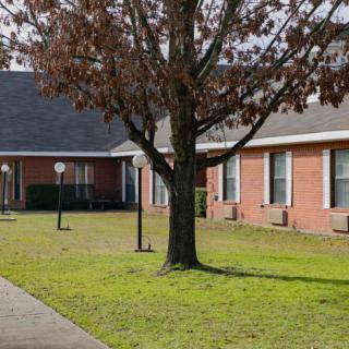 A brick building with large windows surrounded by grass and a tree.