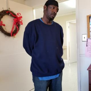 A man standing indoors, wearing a dark sweatshirt and jeans.