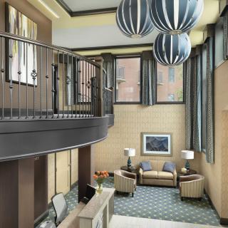 A modern lobby interior featuring a seating area, decorative lighting fixtures, and an upper-level balcony.
