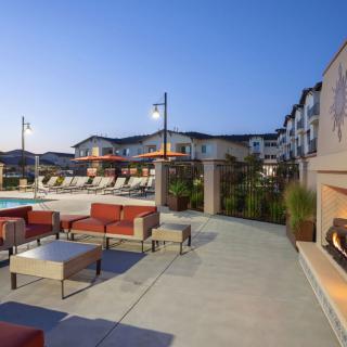 An outdoor seating area with a view of a pool at an apartment complex in the evening.