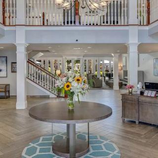 A spacious and elegantly decorated lobby with a central table adorned with flowers and a grand chandelier overhead.