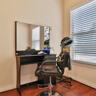 A minimalist hair salon setup featuring a styling chair, mirror, and hair dryer next to a window with blinds.
