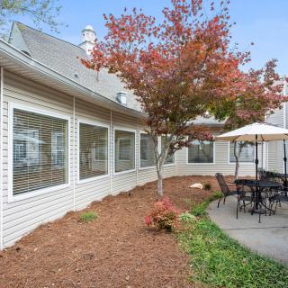 A peaceful patio area with outdoor seating and a tree with autumn foliage, adjacent to a building.