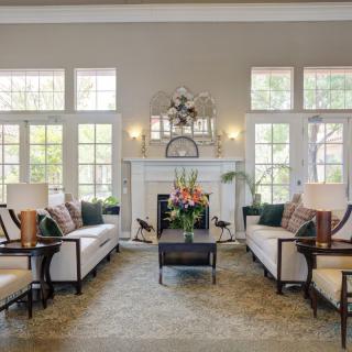 A spacious and elegant living room with large windows, cozy sofas, a central coffee table, and a decorative fireplace.