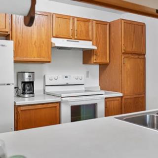 A modern kitchen with wooden cabinets, a white countertop, and essential appliances including a stove, oven, and coffee maker.