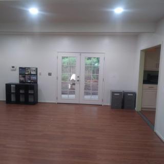 A spacious living room with wooden flooring, minimalist decor, and French doors leading outside.