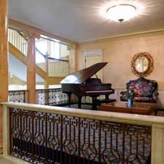 A beautifully designed interior featuring a grand piano, ornate furniture, and a decorative mirror next to a staircase.