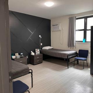 A clean and minimalist hospital room featuring two beds, a chair, and a bedside table.