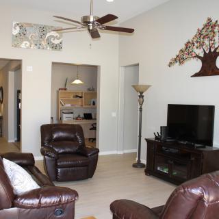 A cozy living room with leather chairs, a TV, ceiling fan, and decorative wall art.