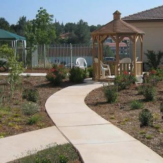 A garden pathway leading to a gazebo with chairs, surrounded by landscaping.