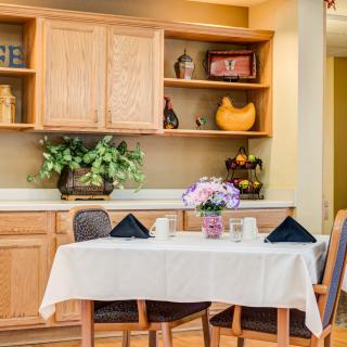 A cozy dining area with a table set for two, featuring a floral centerpiece and surrounded by wooden cabinets.
