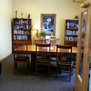 A cozy office meeting room with bookshelves and a central wooden table surrounded by chairs.