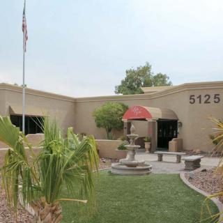 A beige building with an entrance featuring a red canopy, surrounded by landscaping and a fountain in front.