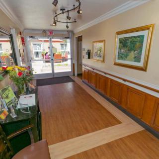 A bright hallway with wooden flooring, adorned with artwork and flowers, leading to a glass doorway.
