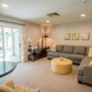 A cozy living room with modern furnishings, featuring a grey sofa, a round yellow ottoman, and large sliding glass doors.