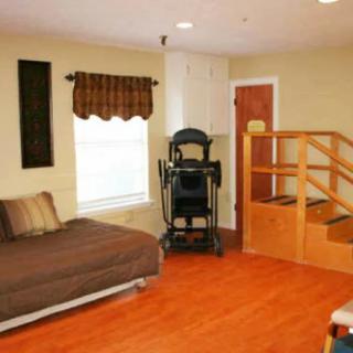 A cozy room with a bed, wooden flooring, a small staircase, and exercise equipment.