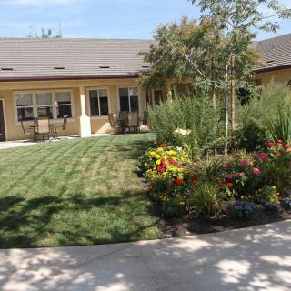 A well-maintained garden with colorful flowers and a lush lawn in front of a house.