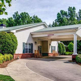 A view of a building entrance with a covered driveway and surrounding greenery.