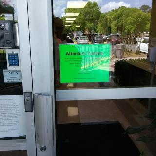 A glass entrance door with a green sign, reflecting the outside view.