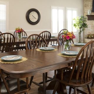A dining room with wooden tables and chairs, decorated with place settings and flower arrangements.