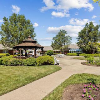 A serene outdoor garden featuring a gazebo, walking paths, and lush greenery under a bright blue sky.