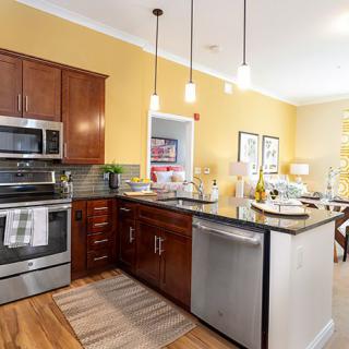 A modern kitchen with stainless steel appliances and wooden cabinets, featuring an island countertop and pendant lighting.