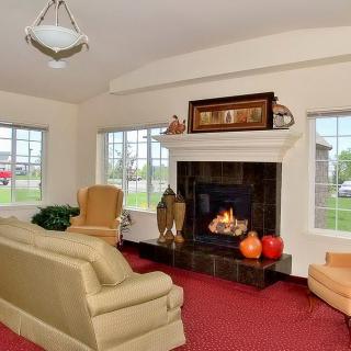 A cozy living room with a lit fireplace, sofa, and bright windows.