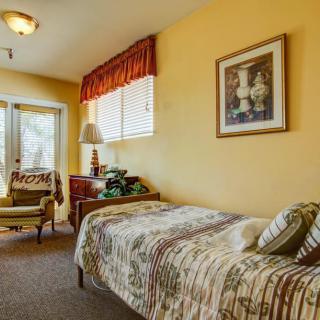 A cozy bedroom with a single bed, a chair by the window, and warm decor.