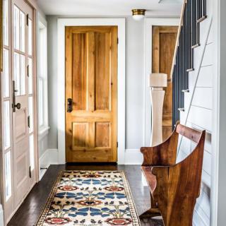 A cozy hallway featuring a wooden door, patterned rug, and a wooden bench alongside a staircase.