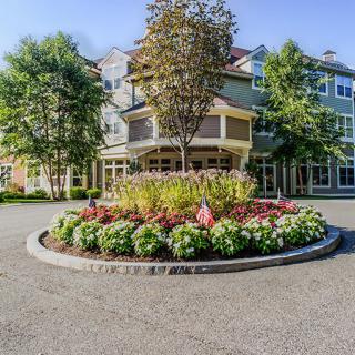 A well-maintained building with a landscaped roundabout featuring flowers and trees.
